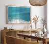 Aerial beach wall art featuring a lone surfer paddling through turquoise ocean waves, with foamy white surf along the shoreline.