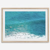 Aerial beach wall art featuring a lone surfer paddling through turquoise ocean waves, with foamy white surf along the shoreline.
