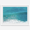 Aerial beach wall art featuring a lone surfer paddling through turquoise ocean waves, with foamy white surf along the shoreline.