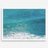 Aerial beach wall art featuring a lone surfer paddling through turquoise ocean waves, with foamy white surf along the shoreline.