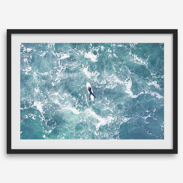 Fine art aerial photography print of a lone surfer floating on a surfboard amidst turquoise ocean waves with intricate white foam patterns.
