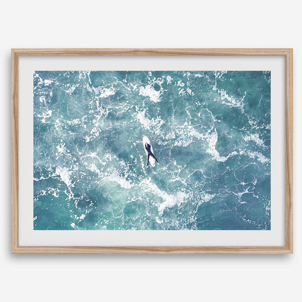 Fine art aerial photography print of a lone surfer floating on a surfboard amidst turquoise ocean waves with intricate white foam patterns.