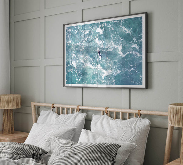 Fine art aerial photography print of a lone surfer floating on a surfboard amidst turquoise ocean waves with intricate white foam patterns.