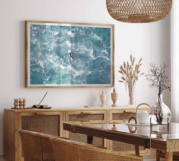Fine art aerial photography print of a lone surfer floating on a surfboard amidst turquoise ocean waves with intricate white foam patterns.
