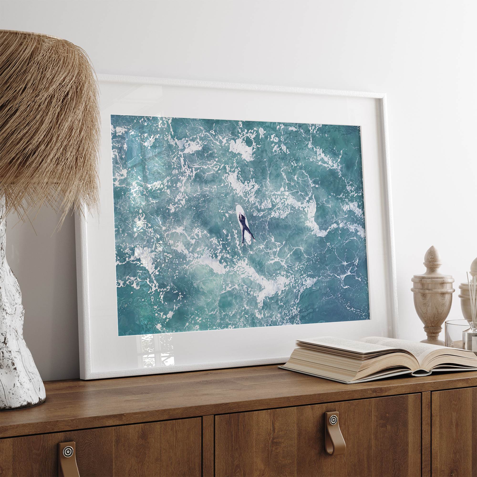 Fine art aerial photography print of a lone surfer floating on a surfboard amidst turquoise ocean waves with intricate white foam patterns.