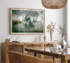 Fine art photography of a misty forest in Alaska, with the tops of trees on a mountain shrouded in white dreamlike fog.