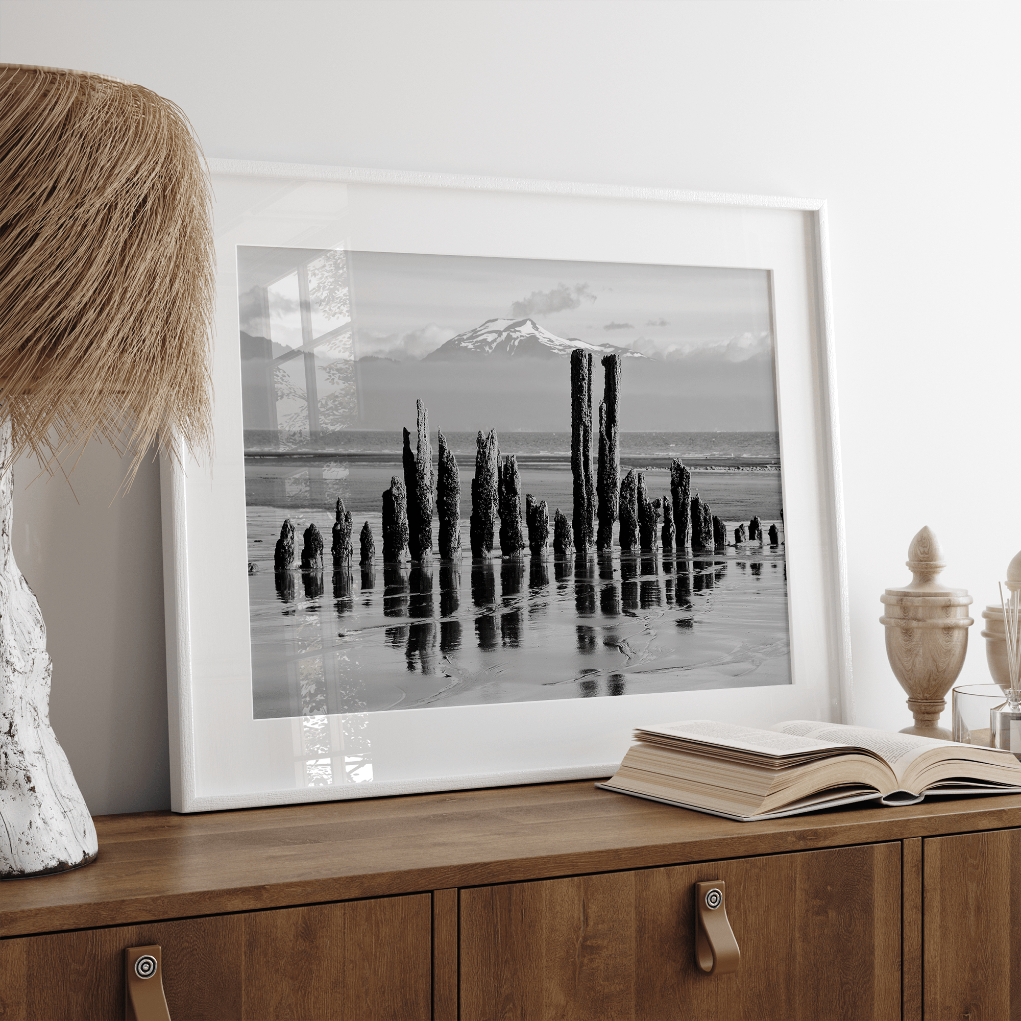 Black and white photo of weathered pilings on an Alaskan beach with snow-capped mountains in the background – fine art print.