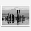 Black and white photo of weathered pilings on an Alaskan beach with snow-capped mountains in the background – fine art print.