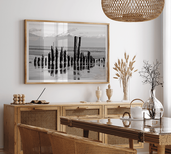 Black and white photo of weathered pilings on an Alaskan beach with snow-capped mountains in the background – fine art print.
