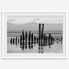Black and white photo of weathered pilings on an Alaskan beach with snow-capped mountains in the background – fine art print.