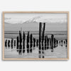 Black and white photo of weathered pilings on an Alaskan beach with snow-capped mountains in the background – fine art print.