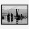 Black and white photo of weathered pilings on an Alaskan beach with snow-capped mountains in the background – fine art print.