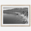 A fine art black and white Lake Tahoe print showcasing docks and boats nested on the lake waters on the left, while the beachfront, nestled against a backdrop of a lush forest and majestic mountain, paints a picturesque scene on the right.