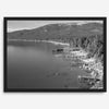 A fine art black and white Lake Tahoe print showcasing docks and boats nested on the lake waters on the left, while the beachfront, nestled against a backdrop of a lush forest and majestic mountain, paints a picturesque scene on the right.