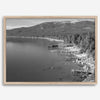A fine art black and white Lake Tahoe print showcasing docks and boats nested on the lake waters on the left, while the beachfront, nestled against a backdrop of a lush forest and majestic mountain, paints a picturesque scene on the right.