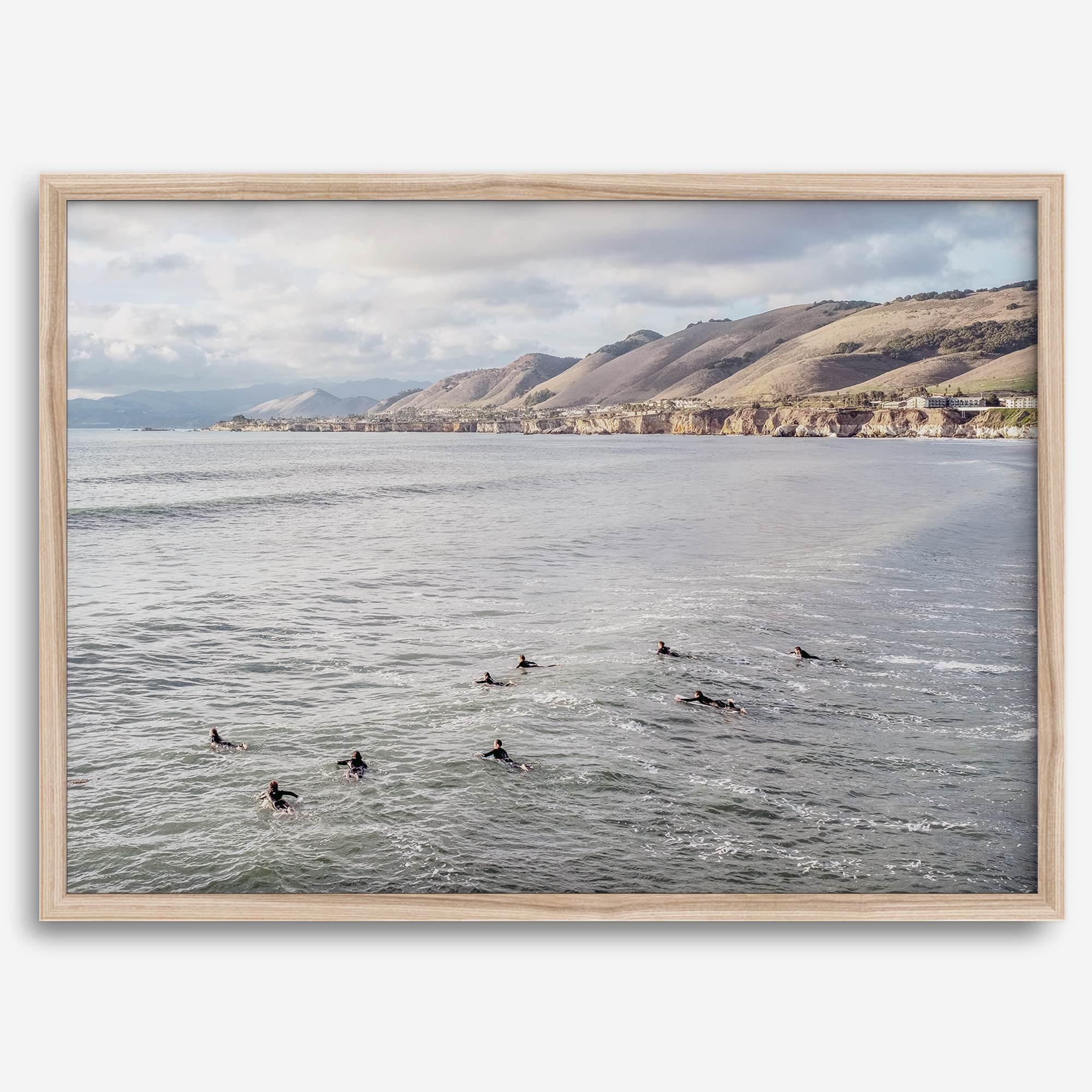 Surfers paddling near Pismo Beach captured in a fine art photography print with coastal cliffs and serene ocean views.