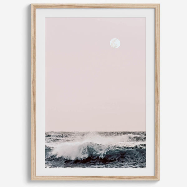 This extraordinary ocean wall art captures a mesmerizing moment when a powerful wave crashes while the sunset gentle blush pink hues fill the sky and a large full moon rises majestically in the backdrop.