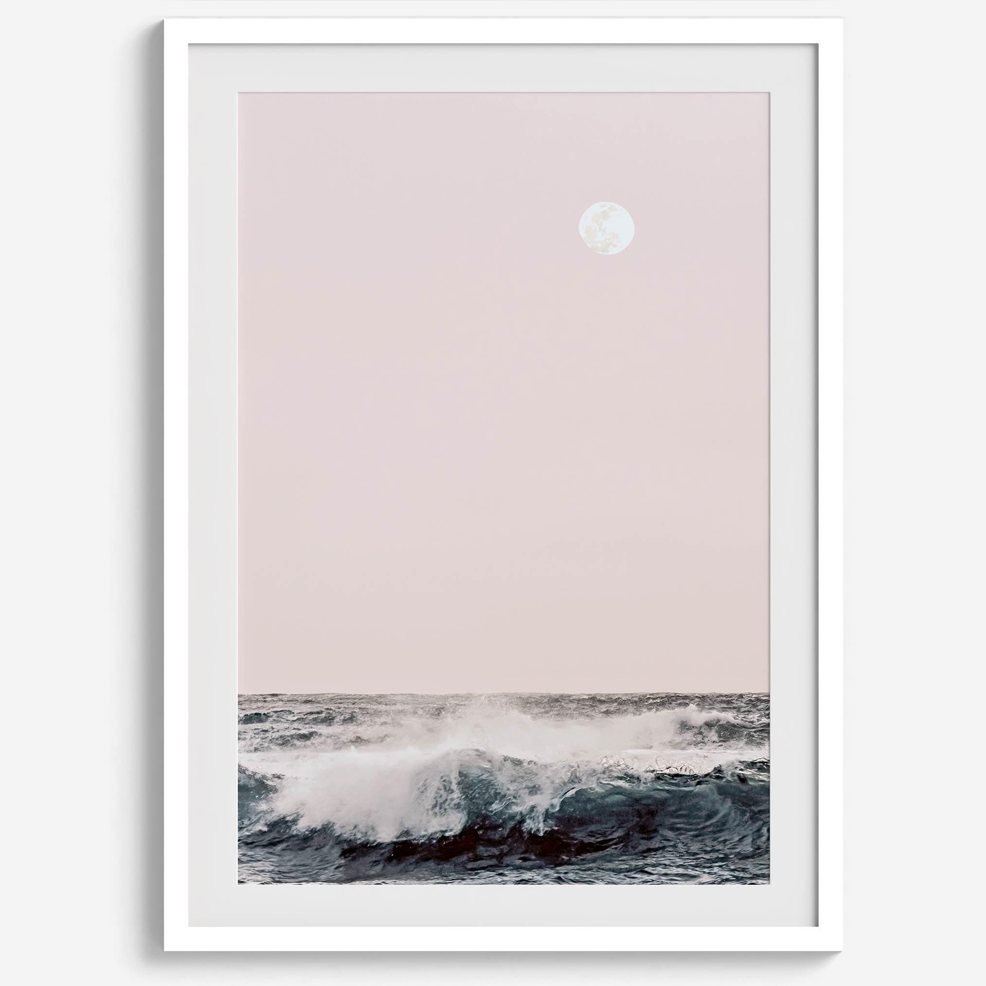 This extraordinary ocean wall art captures a mesmerizing moment when a powerful wave crashes while the sunset gentle blush pink hues fill the sky and a large full moon rises majestically in the backdrop.