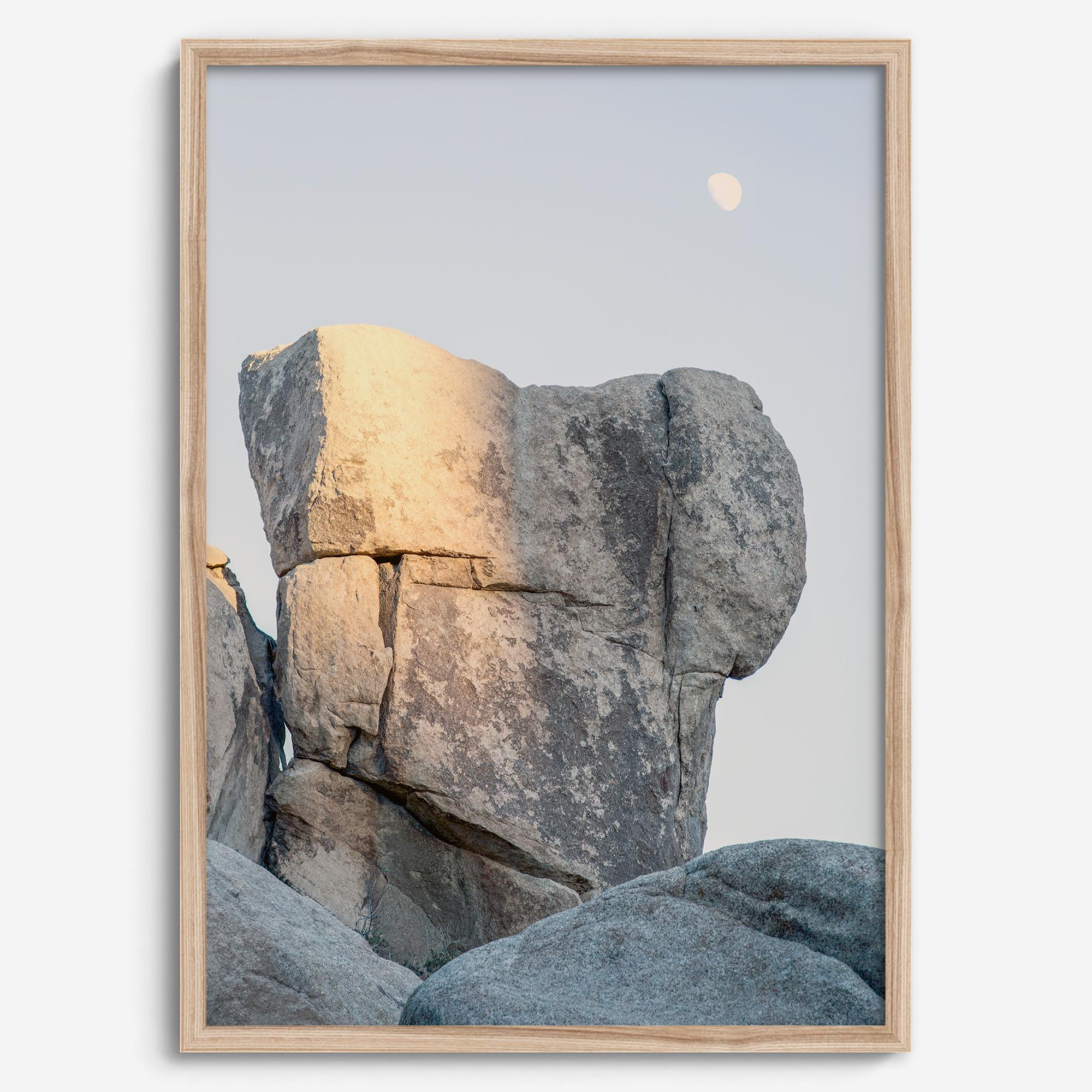 Minimalist desert moon wall art featuring massive sunlit rock formations beneath a pale moon and soft gray sky. Southwest fine art photography.