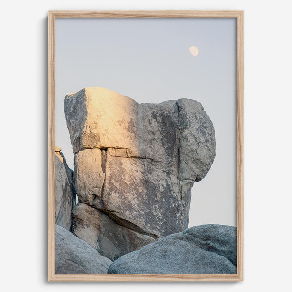 Minimalist desert moon wall art featuring massive sunlit rock formations beneath a pale moon and soft gray sky. Southwest fine art photography.