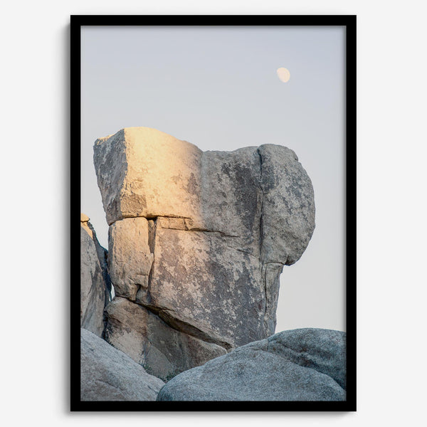 Minimalist desert moon wall art featuring massive sunlit rock formations beneath a pale moon and soft gray sky. Southwest fine art photography.