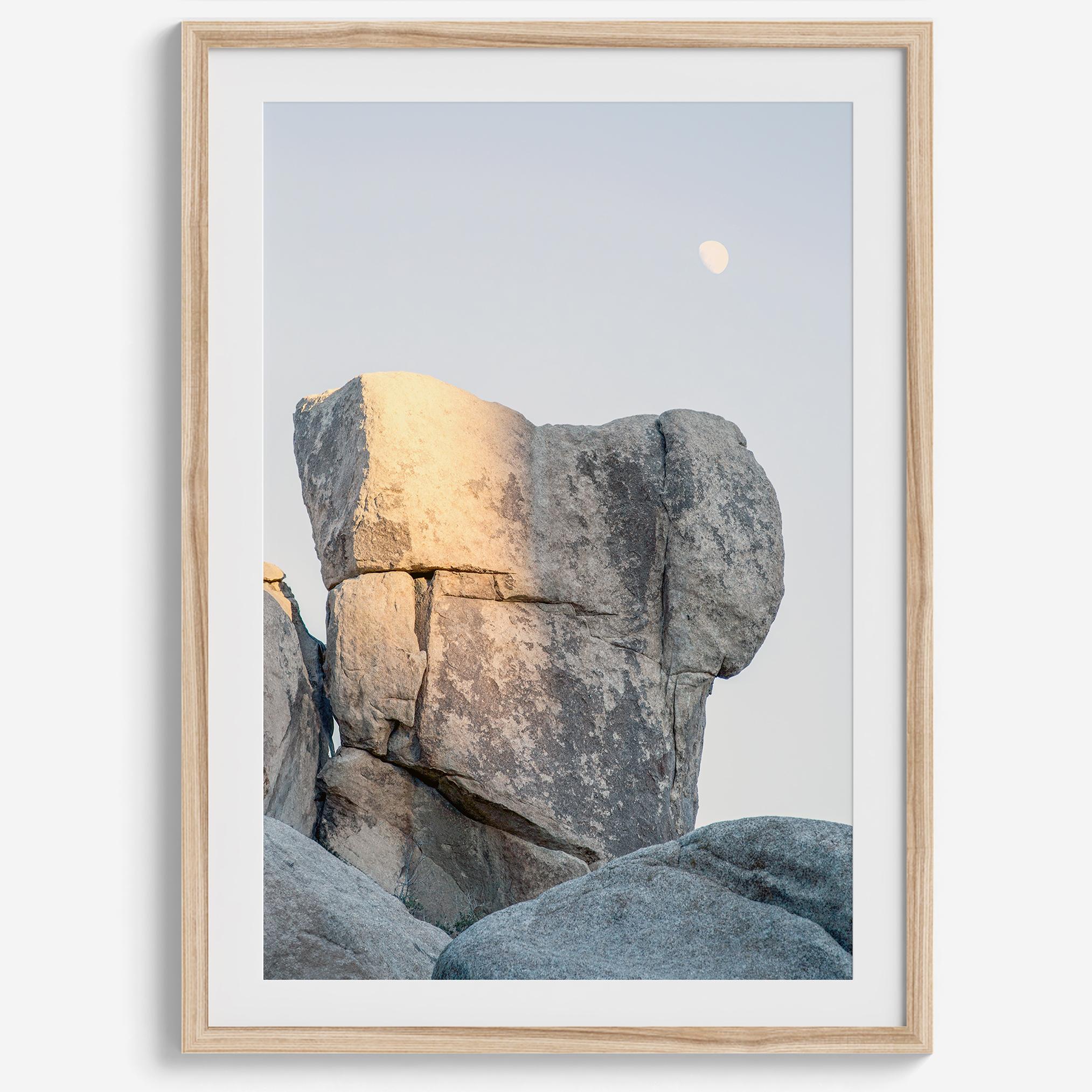 Minimalist desert moon wall art featuring massive sunlit rock formations beneath a pale moon and soft gray sky. Southwest fine art photography.
