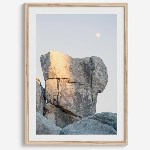 Minimalist desert moon wall art featuring massive sunlit rock formations beneath a pale moon and soft gray sky. Southwest fine art photography.