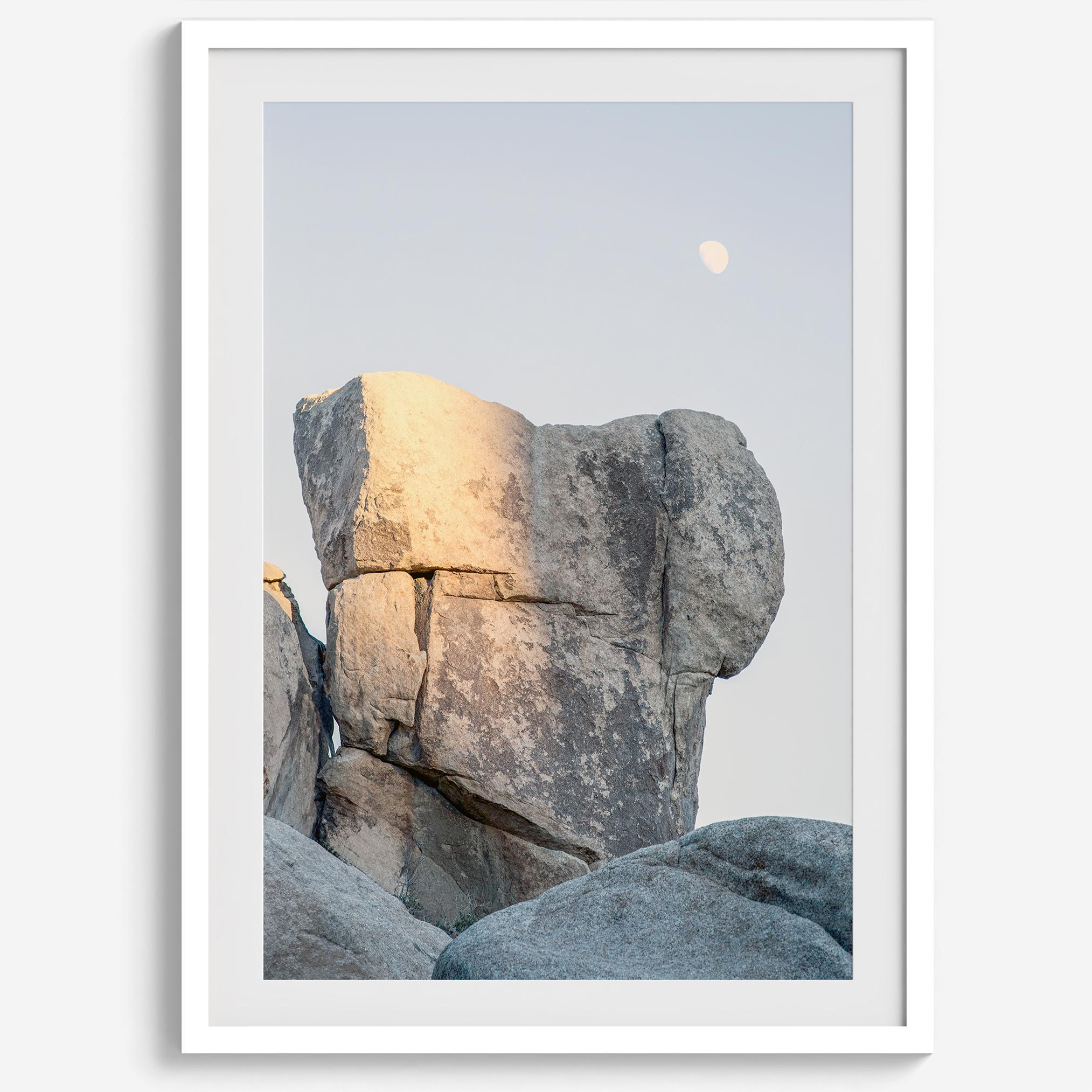 Minimalist desert moon wall art featuring massive sunlit rock formations beneath a pale moon and soft gray sky. Southwest fine art photography.