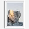 Minimalist desert moon wall art featuring massive sunlit rock formations beneath a pale moon and soft gray sky. Southwest fine art photography.