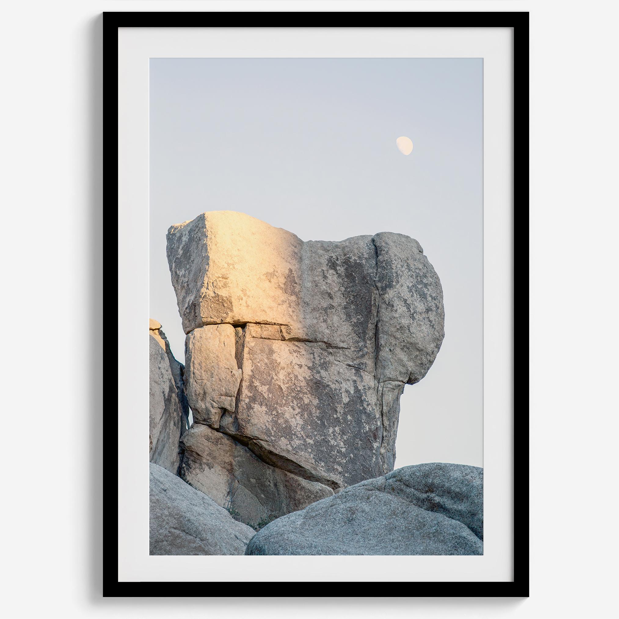 Minimalist desert moon wall art featuring massive sunlit rock formations beneath a pale moon and soft gray sky. Southwest fine art photography.