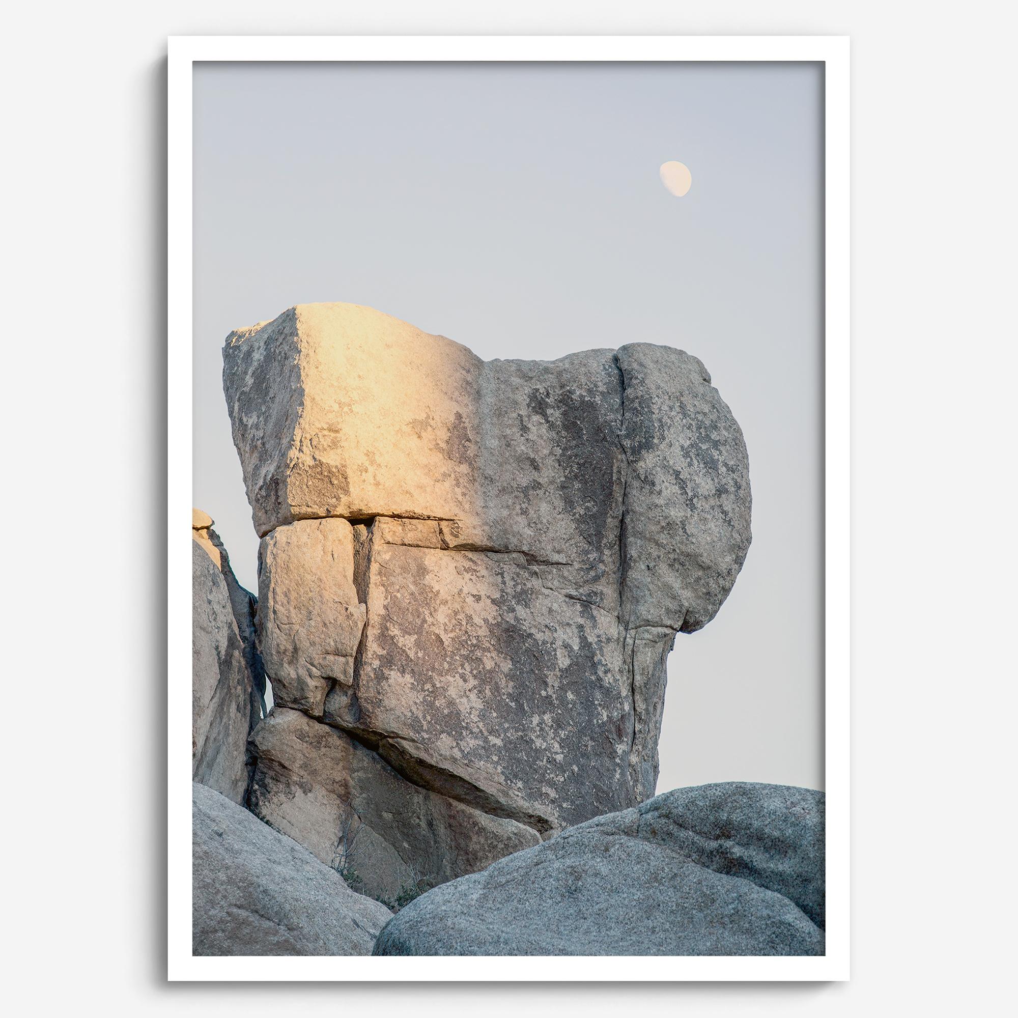 Minimalist desert moon wall art featuring massive sunlit rock formations beneath a pale moon and soft gray sky. Southwest fine art photography.