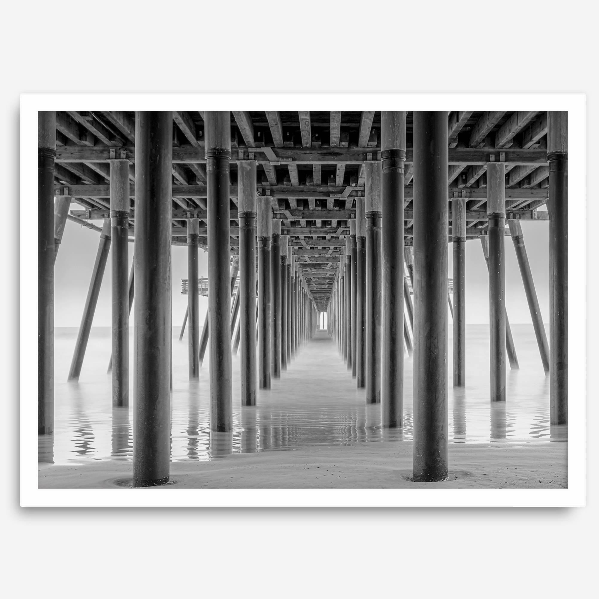 A large fine art abstract black and white beach pier print This stunning beach wall art shows the symmetric structure of the pier with the ocean water gently caressing the pier and beach.