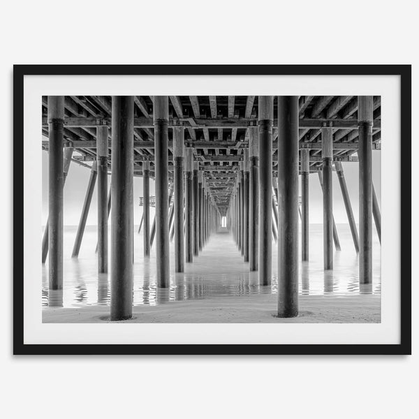 A large fine art abstract black and white beach pier print This stunning beach wall art shows the symmetric structure of the pier with the ocean water gently caressing the pier and beach.