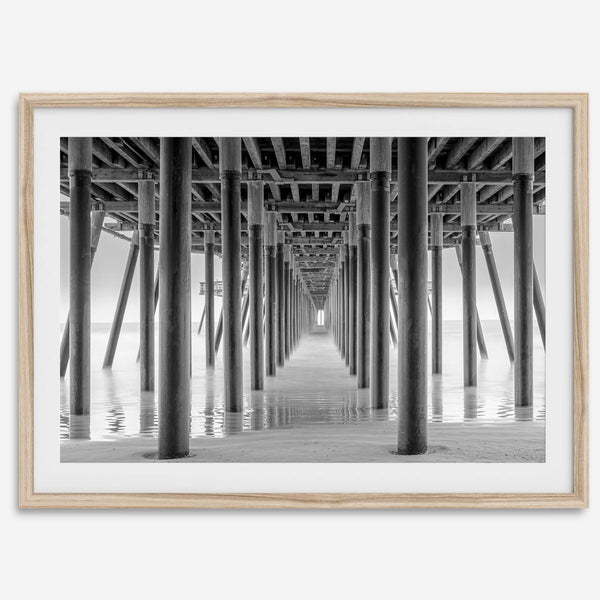 A large fine art abstract black and white beach pier print This stunning beach wall art shows the symmetric structure of the pier with the ocean water gently caressing the pier and beach.