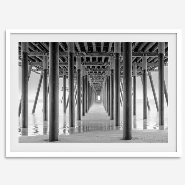 A large fine art abstract black and white beach pier print This stunning beach wall art shows the symmetric structure of the pier with the ocean water gently caressing the pier and beach.