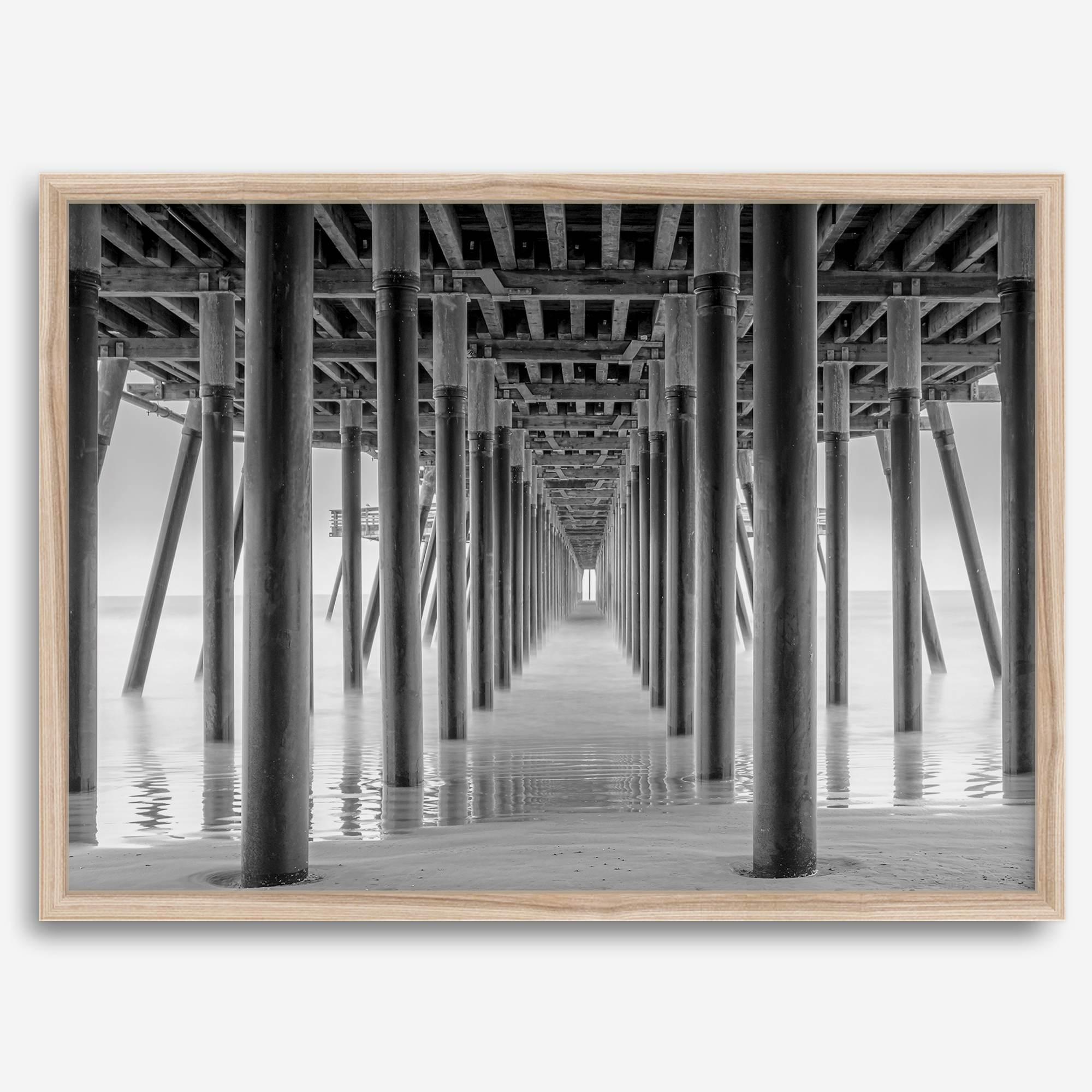A large fine art abstract black and white beach pier print This stunning beach wall art shows the symmetric structure of the pier with the ocean water gently caressing the pier and beach.
