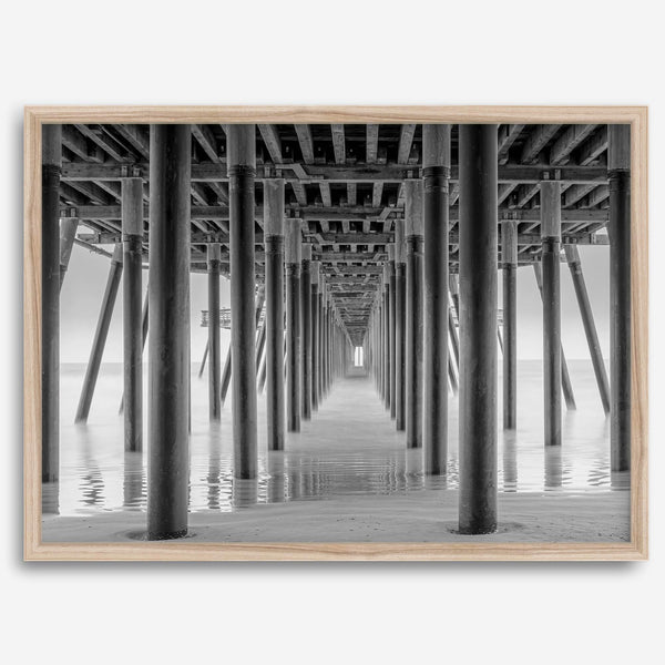 A large fine art abstract black and white beach pier print This stunning beach wall art shows the symmetric structure of the pier with the ocean water gently caressing the pier and beach.