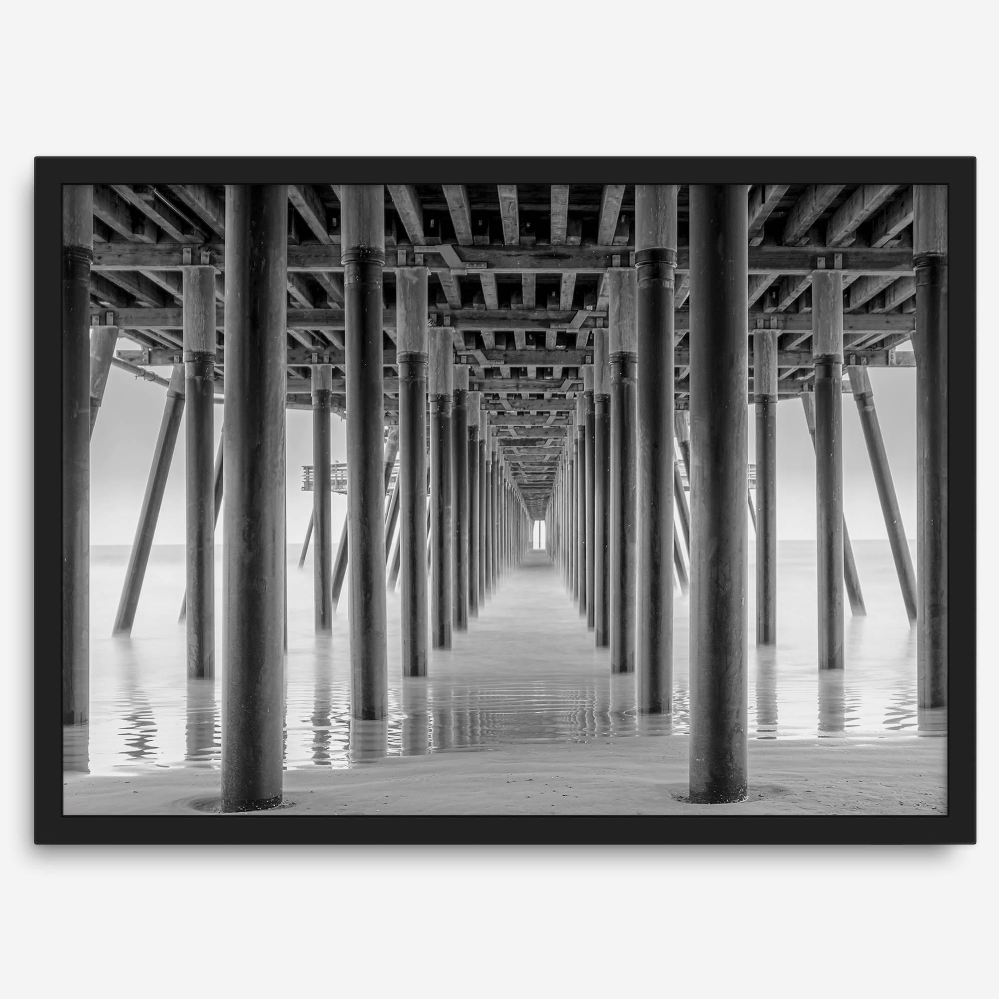 A large fine art abstract black and white beach pier print This stunning beach wall art shows the symmetric structure of the pier with the ocean water gently caressing the pier and beach.