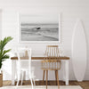 A fine art photography print capturing a female surfer walking back from the ocean at sunset with waves breaking in the foreground, capturing the end of a surf session.