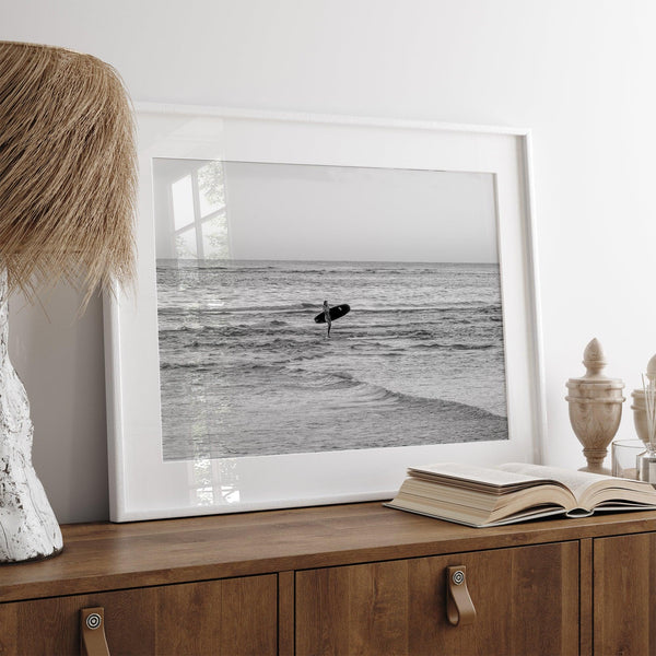 A fine art photography print capturing a female surfer walking back from the ocean at sunset with waves breaking in the foreground, capturing the end of a surf session.