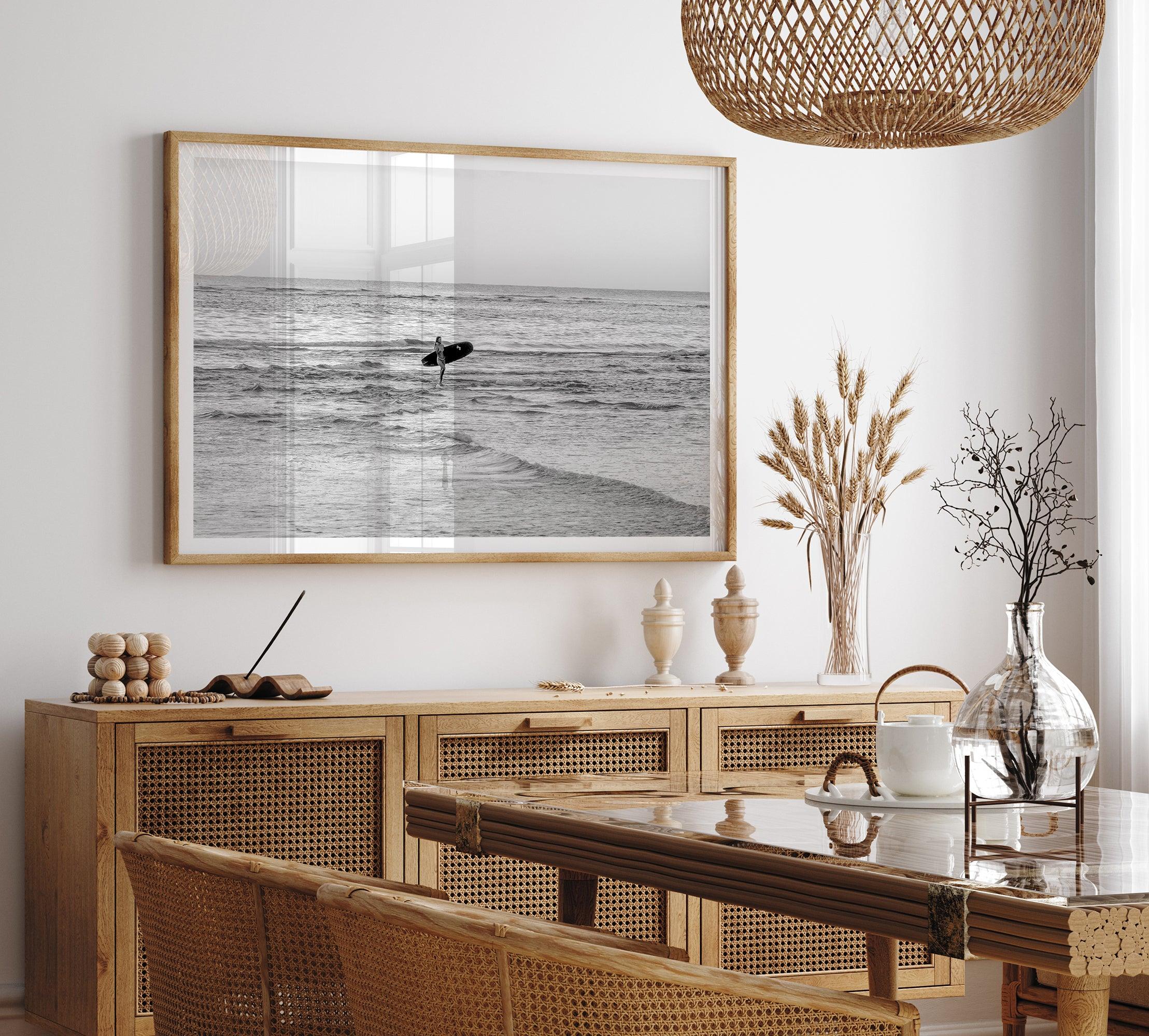 A fine art photography print capturing a female surfer walking back from the ocean at sunset with waves breaking in the foreground, capturing the end of a surf session.