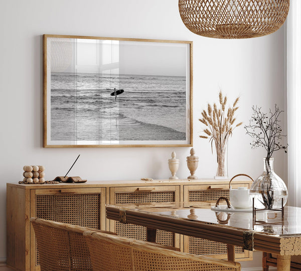 A fine art photography print capturing a female surfer walking back from the ocean at sunset with waves breaking in the foreground, capturing the end of a surf session.