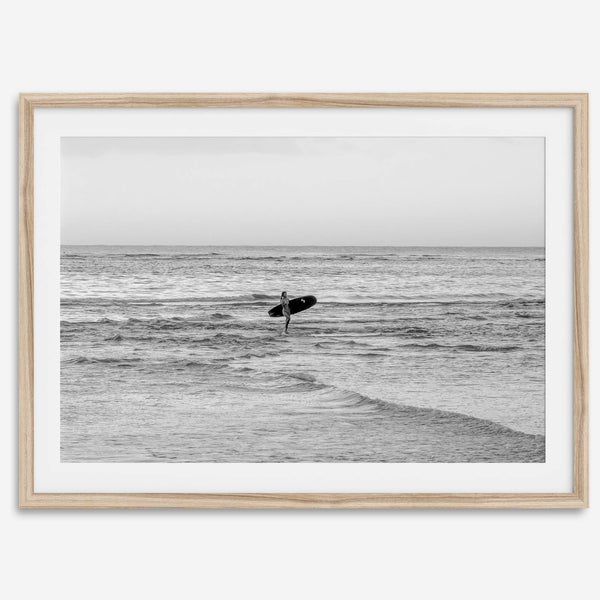 A fine art photography print capturing a female surfer walking back from the ocean at sunset with waves breaking in the foreground, capturing the end of a surf session.