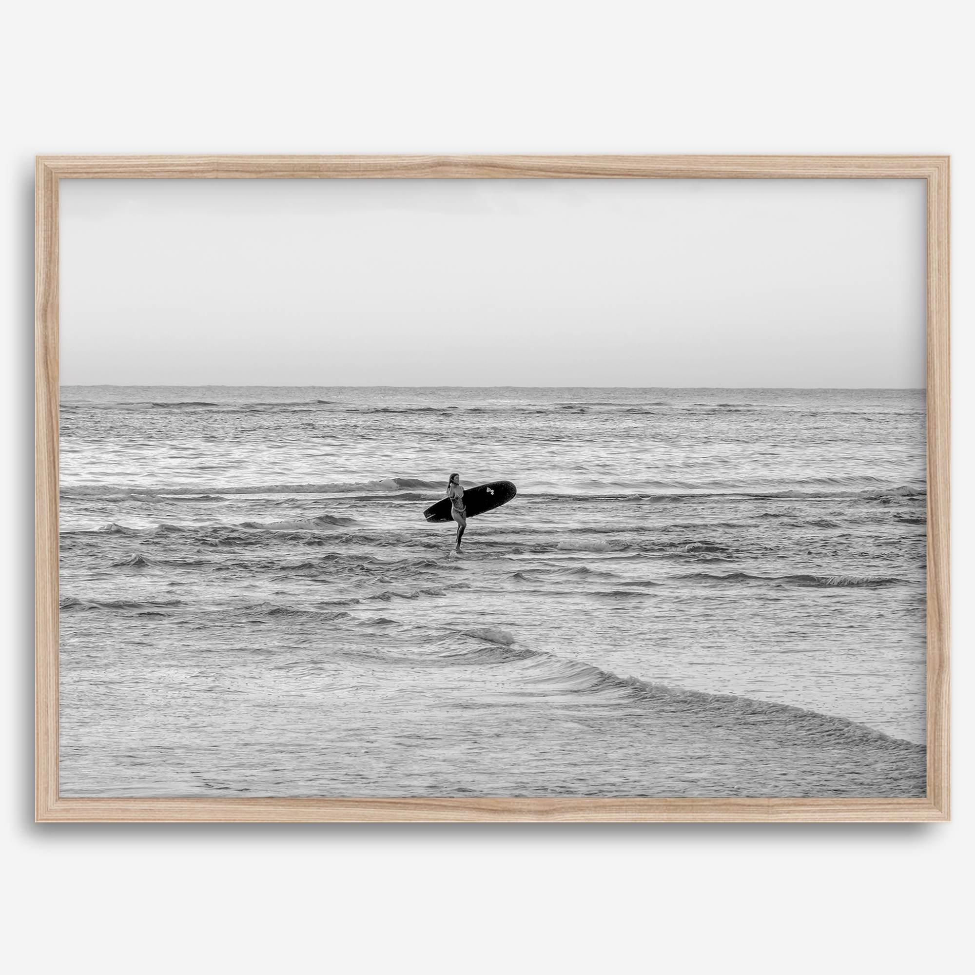 A fine art photography print capturing a female surfer walking back from the ocean at sunset with waves breaking in the foreground, capturing the end of a surf session.