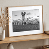 Black and white photo of the Pismo Beach street sign with palm trees and boardwalk – fine art coastal print