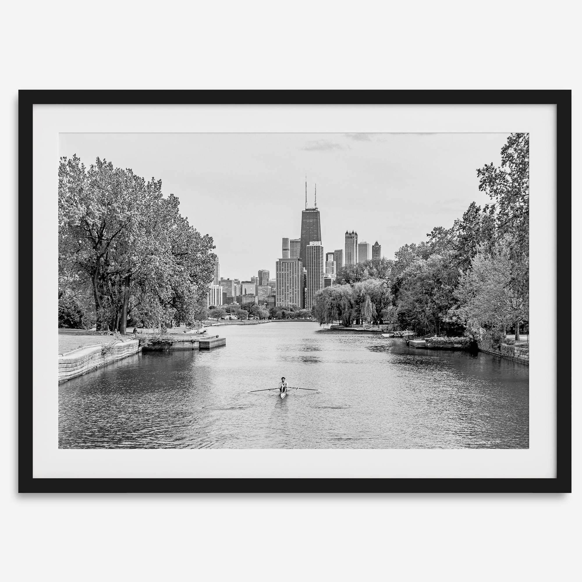 Black and white photo of Lincoln Park, Chicago. A lone rower glides on the park canal with the iconic Willis Tower (formerly Sears Tower) and Chicago skyline in the background.
