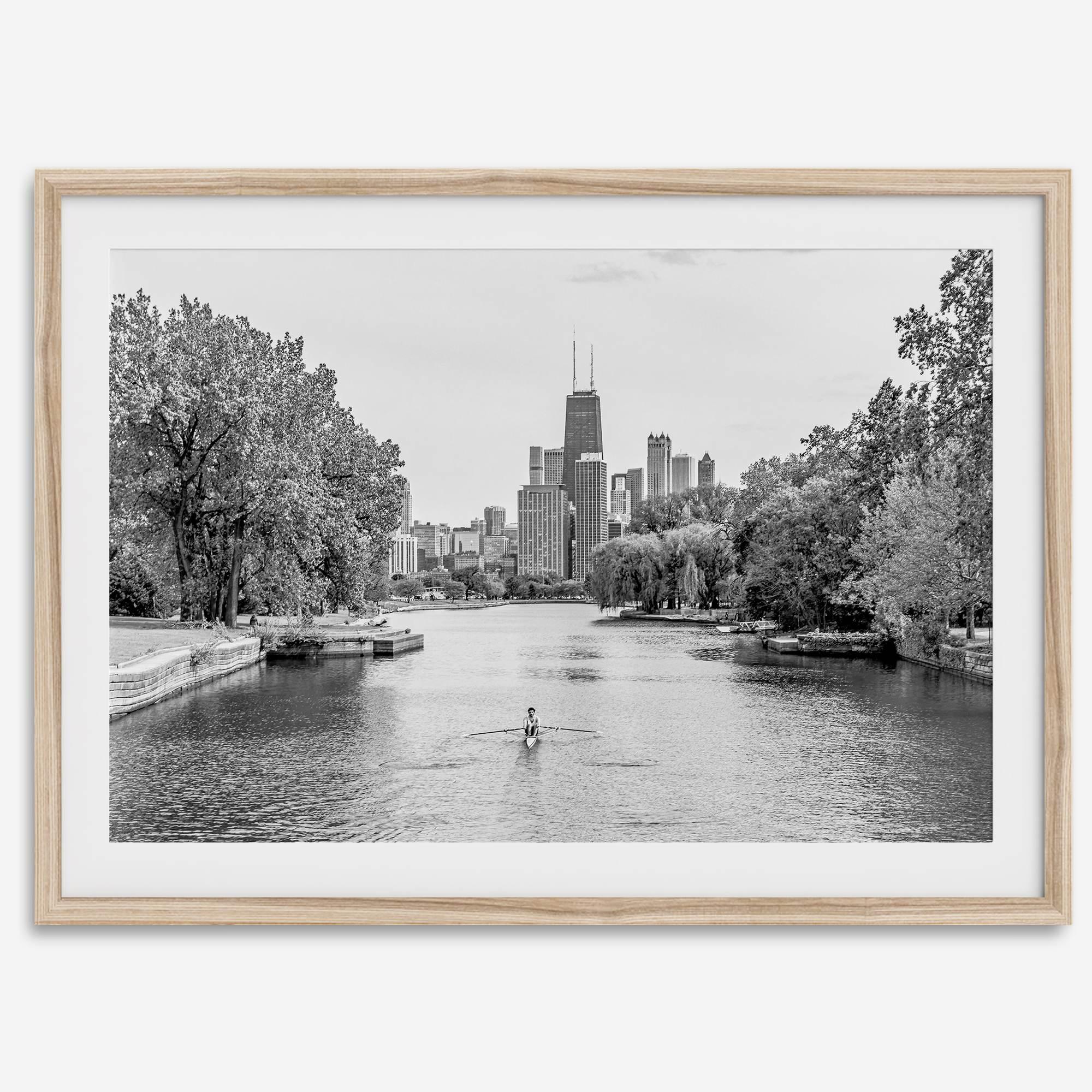 Black and white photo of Lincoln Park, Chicago. A lone rower glides on the park canal with the iconic Willis Tower (formerly Sears Tower) and Chicago skyline in the background.