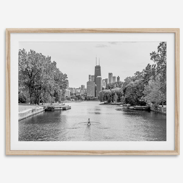 Black and white photo of Lincoln Park, Chicago. A lone rower glides on the park canal with the iconic Willis Tower (formerly Sears Tower) and Chicago skyline in the background.