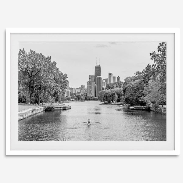 Black and white photo of Lincoln Park, Chicago. A lone rower glides on the park canal with the iconic Willis Tower (formerly Sears Tower) and Chicago skyline in the background.