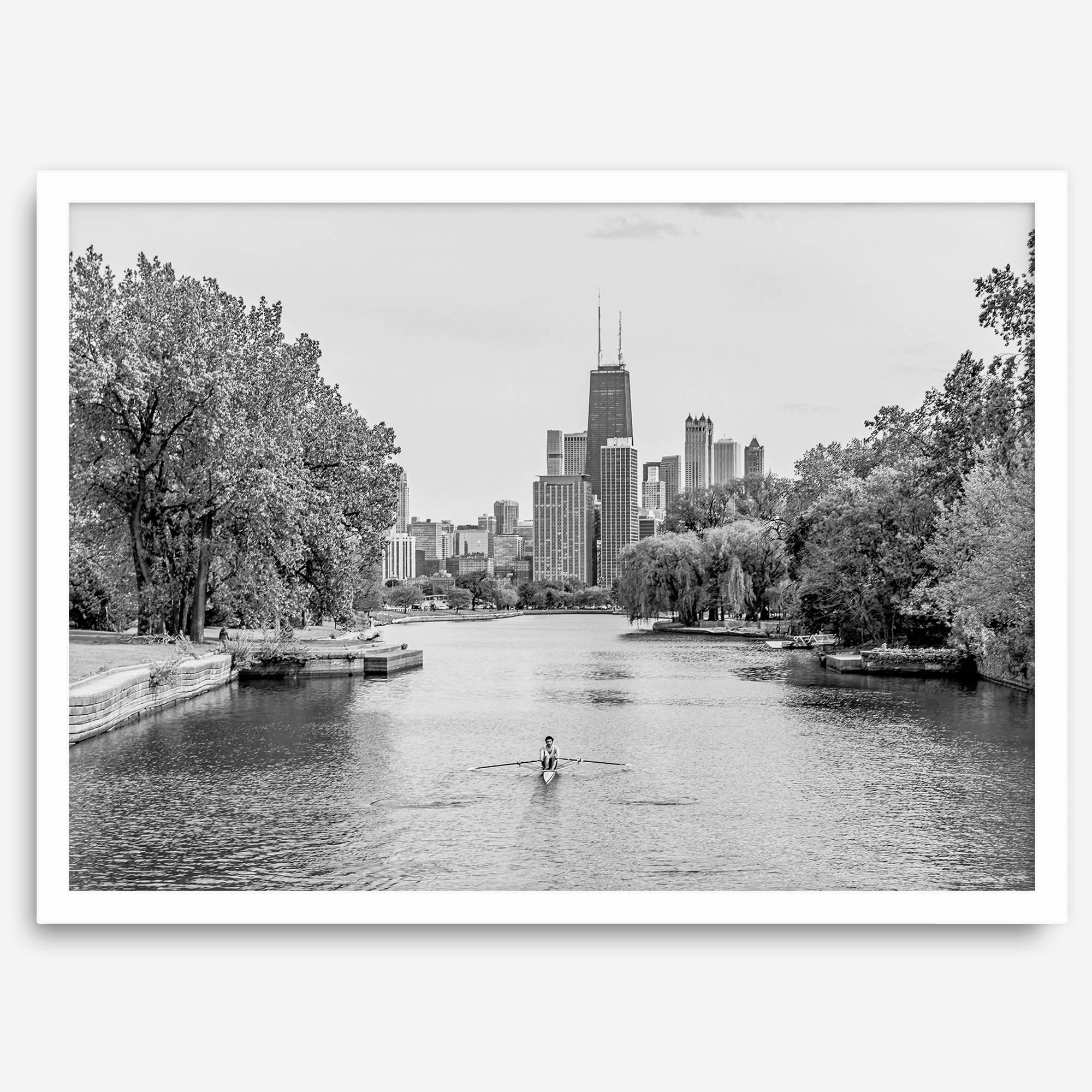 Black and white photo of Lincoln Park, Chicago. A lone rower glides on the park canal with the iconic Willis Tower (formerly Sears Tower) and Chicago skyline in the background.